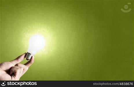 Glowing electric bulb . Hand holding glass glowing lightbulb on green background