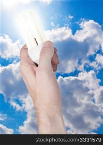 Glowing Energy Saving Bulb in Hand on Blue Sky Background