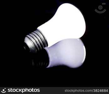 Glowing halogen bulb not in socket, with reflection on black surface