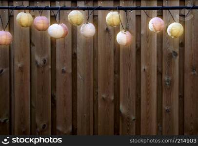 Glowing lanterns lampion lights with delicate design hanging wooden fence,decorative stylish design with copy space. cozy garden decoration space for text. Glowing lanterns lampion lights with delicate design hanging wooden fence,decorative stylish design with copy space. cozy garden decoration