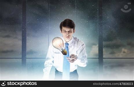 Glowing light bulb. Young businessman examining glass glowing light bulb