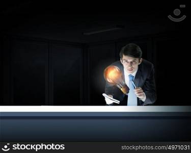 Glowing light bulb. Young businessman examining glass glowing light bulb