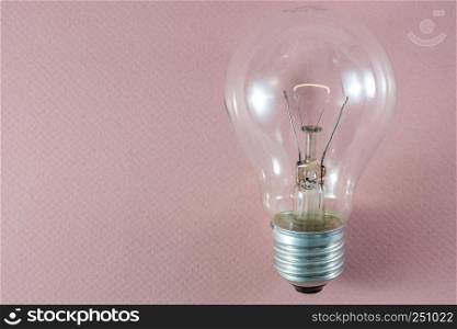 Glowing tungsten filament light bulb on pink background useful to demonstrate concepts e.g. energy, creativity or idea generation