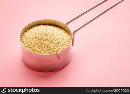 gluten free amaranth grain in a metal measuring scoop against pink background