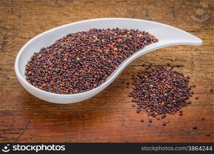 gluten free black quinoa grain grown iin Bolivia , a teardrop shaped bowl against rustic grunge wood