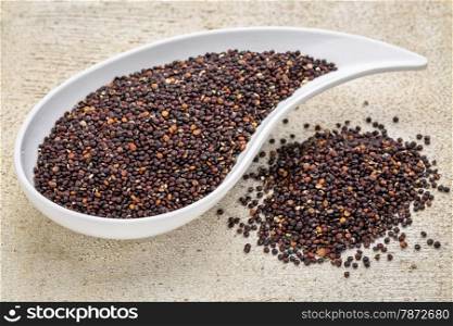 gluten free black quinoa grain grown iin Bolivia , a teardrop shaped bowl against white painted grunge wood