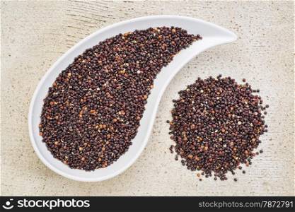 gluten free black quinoa grain grown iin Bolivia , a teardrop shaped bowl against white painted grunge wood, top view