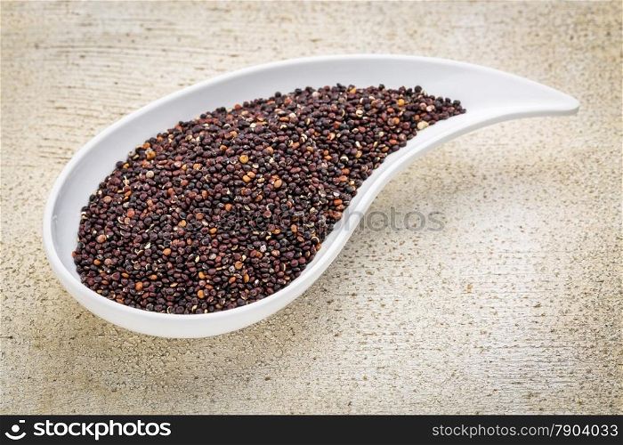 gluten free black quinoa grain grown in Bolivia , a teardrop shaped bowl against white painted grunge wood