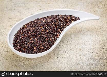gluten free black quinoa grain grown in Bolivia , a teardrop shaped bowl against white painted grunge wood