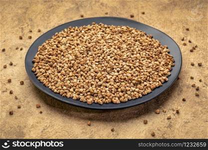 gluten free buckwheat kasha on a black ceramic plate against textured paper background, healthy eating concept