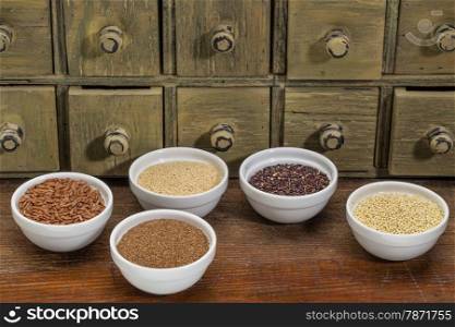gluten free grains (amaranth, millet, quinoa, brown rice, teff in small ceramic bowls with a rustic darwer cabinet in background