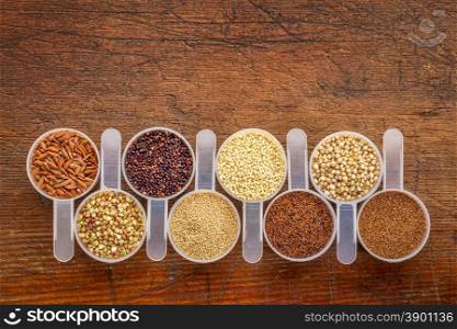 gluten free grains (quinoa, brown rice, kaniwa, amaranth, sorghum, millet, buckwheat, teff) - a row of measuring scoops on a rustic wood with a copy space