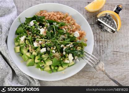 Gluten-free green vegetarian salad made of microgreen sprouts peas, avocado, quinoa, spinach, seasoned crushed almonds with slices of feta cheese