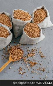 Gluten free product. Vertical shot of dry brown buckwheat for vegetarians. Sacks with cereals. Wooden spoon near. Heathy eating concept