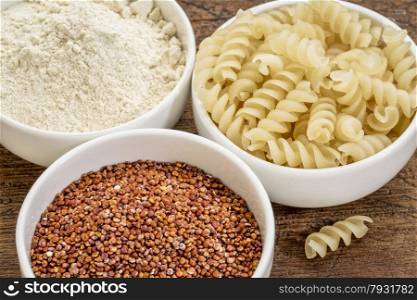gluten free quinoa grain, flour and pasta on small ceramic bowls - healthy eating concept