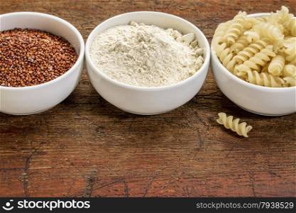 gluten free quinoa grain, flour and pasta - three small ceramic bowls against rustic wood with a copy space