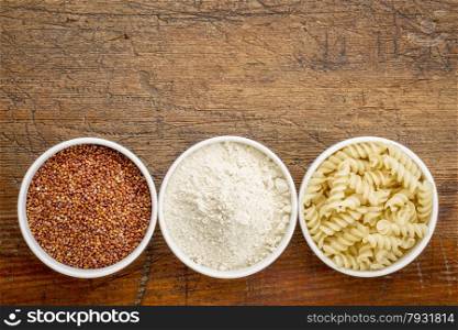 gluten free quinoa grain, flour and pasta - top view of small ceramic bowls against rustic wood with a copy space