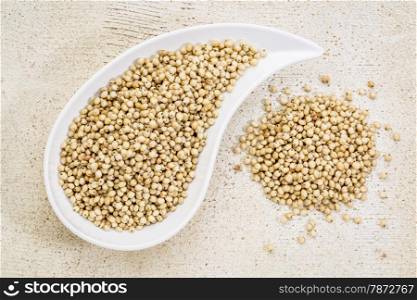 gluten free sorghum grain in a teardrop shaped bowl against white painted grunge wood, top view