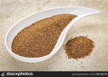 gluten free teff grain on a teardrop shaped bowl against white painted grunge wood