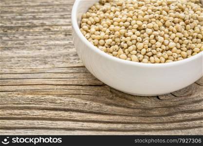 gluten free, white sorghum grain in a small ceramic bowl against grained wood