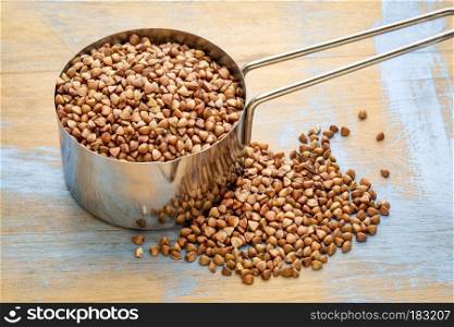 glutn free buckwheat kasha in a measuring scoop  1/4 cup  against wood background