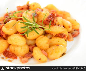 Gnocchi with tomatoes, bacon and onion on the white plate.