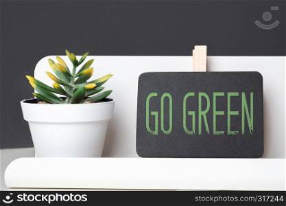 GO green on blackboard and green plant in white pot on table and dark grey wall in office desk.eco office