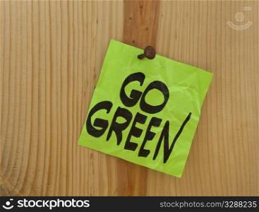 go green reminder - green crumpled sticky note nailed to a wood plank or wall