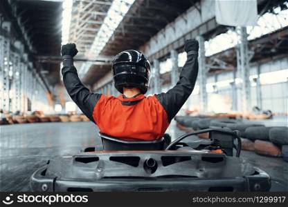 Go kart racer raised his hands up, winner, back view, karting auto sport indoor. Speed race on close go-kart track with tyre barrier. Fast vehicle competition, hot pursuit