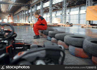 Go kart racer sitting on tires, karting auto sport indoor. Speed race on close go-kart track with tyre barrier. Fast vehicle competition, hot pursuit. Go kart racer sitting on tires, karting auto sport