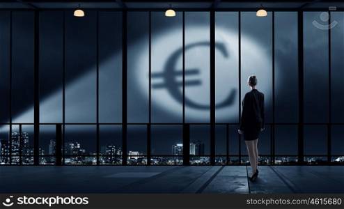 Goal is to become rich. Businesswoman standing with back in darkness and euro sign in spothlight