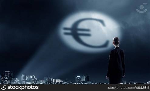 Goal is to become rich. Businesswoman standing with back in darkness and euro sign in spothlight