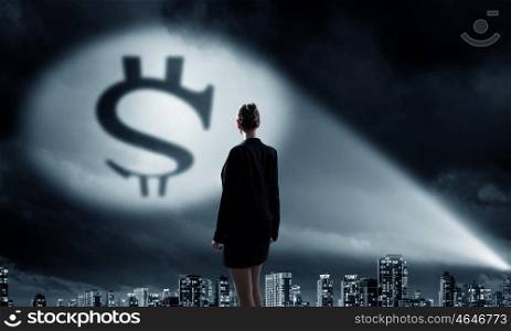Goal is to become rich. Businesswoman standing with back in darkness and dollar sign in spothlight