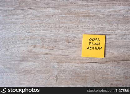 goal, plan and action word on yellow paper note on wooden table background. Strategy, mission, vision concept