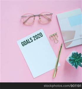 Goals 2020 on flat lay photo of colorful workspace desk with card, eyeglasses and notebook with copy space background, minimal style and mockup concept