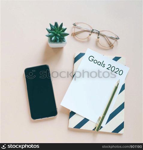 Goals 2020 on flat lay photo of workspace desk with smartphone, card and notebook with copy space background, minimal style and mockup concept