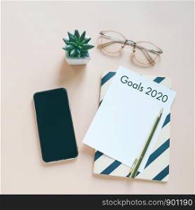 Goals 2020 on flat lay photo of workspace desk with smartphone, card and notebook with copy space background, minimal style and mockup concept