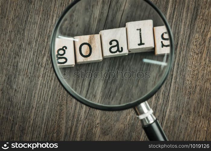 Goals concept key for success in business. Magnifying glass focus on goals word typography over blocks and wooden table background, top view from above,