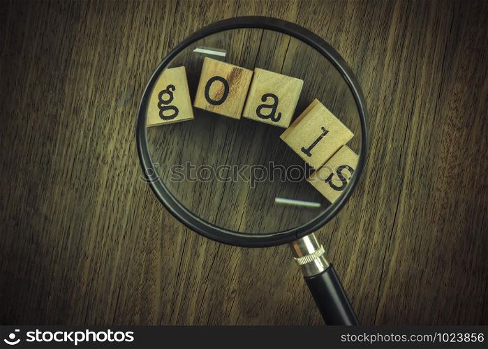 Goals setting strategy for business management. Magnifying glass focus on goals word typography over blocks and wooden table background, vintage and retro style.
