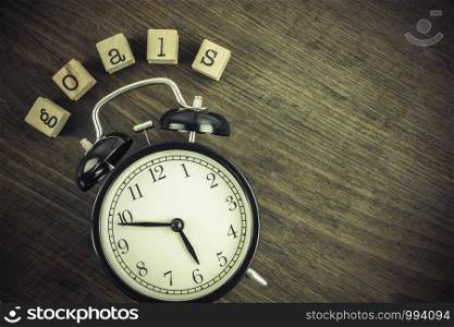 Goals word concept with alarm clock on wooden table texture background, blank space. Text on wooden cube block stampers, vintage retro and flat lay style. Business management ideas.