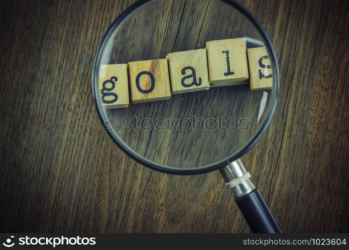 Goals word concept, work improvement and key for success. Goals typography text on a group of cubes under magnifying glass over wooden texture backgroud, vintage style.