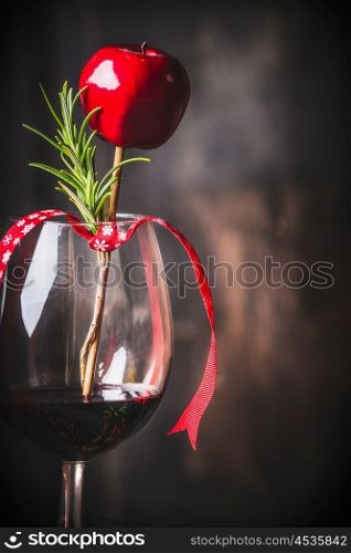 Goblet of red wine with Christmas decoration and rosemary at dark rustic wooden background, close up