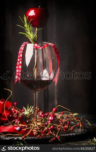Goblet of red wine with festive Christmas decoration and rosemary at dark rustic wooden background, side view