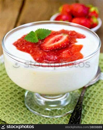 Goblet with a dessert of strawberries and yogurt, spoon on green napkin, strawberries on a wooden boards background