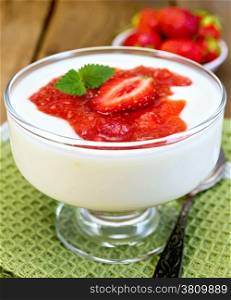 Goblet with a dessert of strawberries and yogurt, spoon on green napkin, strawberries on a wooden boards background