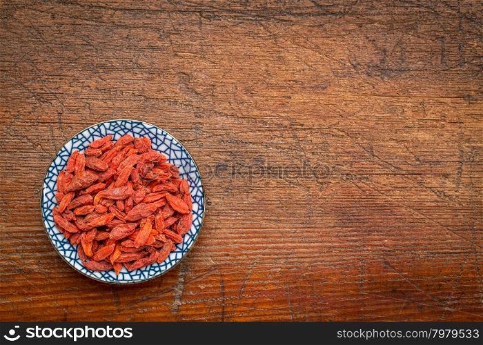 goji berries (woldberry) - small ceramic bowl on a rustic wood with a copy space