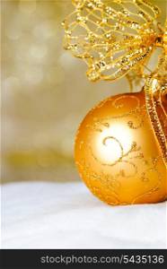 Gold Christmas ball and bow ornament on white fur of defocused golden lights. Shallow DOF.