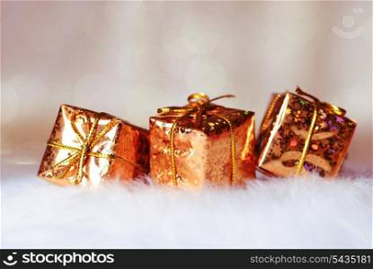 Gold Christmas presents on white fur and background of defocused golden lights. Shallow DOF.
