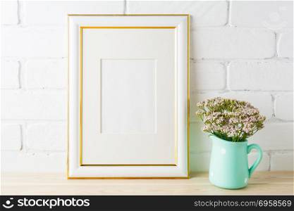 Gold decorated frame mockup with wild very soft pink flowers in mint pitcher near painted brick wall. Empty frame mock up for presentation design. Template framing for modern art.. Gold decorated frame mockup with soft pink flowers and bricks