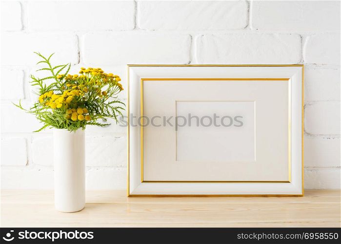 Gold decorated landscape frame mockup with wild deep rich yellow flowers in vase near painted brick walls. Empty frame mock up for presentation design. Template framing for modern art.. Gold decorated landscape frame mockup near painted brick walls